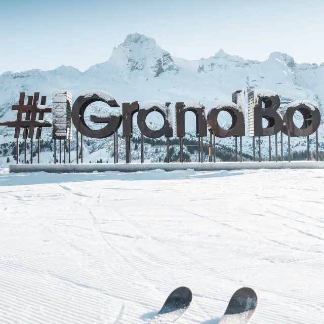 wooden letters with frost form the word mongrandbo in front of the snow-covered aravis range