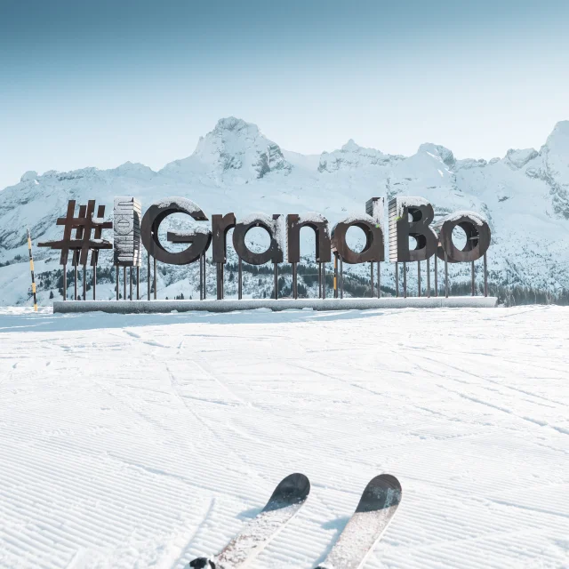des lettres en bois avec du givre forment le mot mongrandbo devant la chaine des aravis enneigée