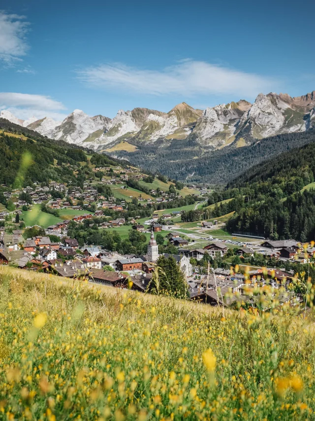 Blick auf das Dorf im Sommer in Le Grand-Bornand mit verschwommenen gelben Blumen im Vordergrund. Schöner Blick auf die Aravis-Kette inmitten grüner Natur.