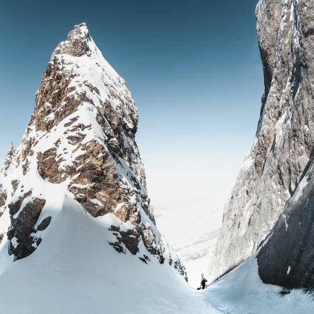 Un skieur en randonnée sort d'un couloir de montagne enneigé dans une atmosphère de grandeur et d'aventure