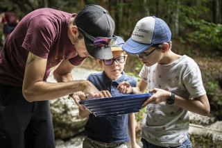 2 enfants et un adulte regardent dans le tamis à la recherche de pépites d'or